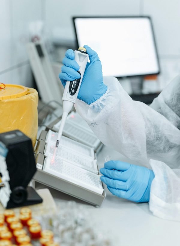 Professional in protective gear using a pipette in a laboratory setting with advanced equipment.